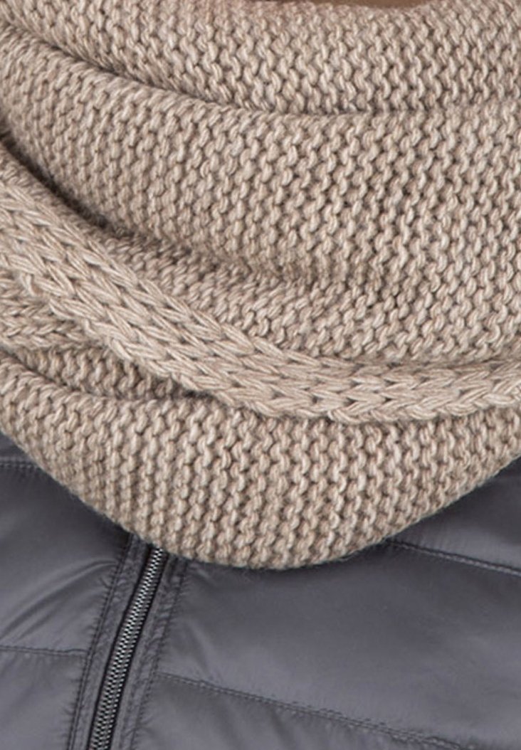 Écharpe beige en maille à infinity avec un motif texturé et épais, superposée sur une doudoune gris foncé avec un détail de fermeture éclair.