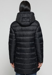 Zwarte pufferjas met een capuchon, voorzien van een doorgestikt design en ribbelstructuur. Lange mouwen en een middellange snit bieden bedekking.