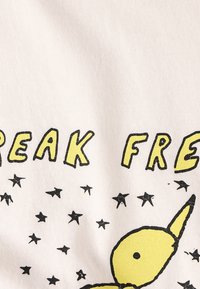 Material din bumbac cu un fundal alb, prezentând stele negre. Textul spune "BREAK FREE" în galben, iar un personaj galben cu urechi lungi.