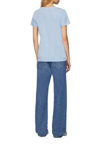 T-shirt azzurro a maniche corte realizzato in tessuto morbido, abbinato a jeans blu a gamba larga. Il T-shirt presenta un classico colletto a girocollo.