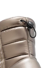 Bota acolchada de color champagne metálico con diseño acolchado, cierre de botón y textura suave. Presenta una puntera ligeramente redondeada y una forma estructurada.