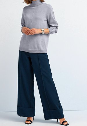 Pullover grigio a collo alto con maniche lunghe abbinato a pantaloni larghi blu navy con risvolto, indossato con sandali neri. Texture liscia.
