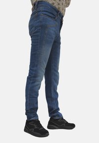 Jeans skinny blu in denim, con un design sbiadito, cinque tasche e vita media. Abbinati a scarpe da ginnastica nere.