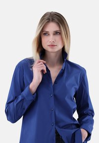 Blue button-up shirt made of smooth fabric, featuring a collar, long sleeves, and visible buttons, displayed with a relaxed fit.