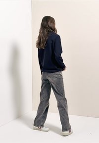 Marineblauwe sweatshirt gecombineerd met grijze oversized jeans, met een ontspannen pasvorm en subtiele distressed textuur, aangevuld met witte sneakers.