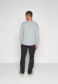 Grau langärmliges Shirt und schwarze Hose, beide mit entspannter Passform. Das Shirt hat einen runden Halsausschnitt; die Hose ist knöchellang und hat seitliche Reißverschlüsse.