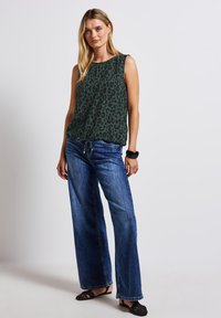 Tmavě zelený bezrukávový top s leopardím potiskem, zkombinovaný s širokými modrými džíny a černými sandály. Obsahuje stahovací prvek na lemu.