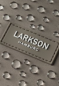Szürke szövet anyag, különböző méretű megemelkedett cseppekkel. Tartalmaz egy téglalap alakú címkét, rajta "LARKSON HAMBURG" felirattal fehér betűkkel.