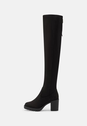Botte haute noire pour femme jusqu'au genou avec talon épais et bout rond, fermeture éclair latérale et semelle crantée sur fond blanc.