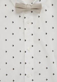 Fehér ing kis fekete és bézs gyémánt alakú geometriai mintával. Klasszikus gallérral és világosszürke csokornyakkendővel rendelkezik. A gombok fehérek.