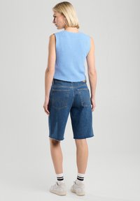 Light blue knitted sleeveless top paired with denim shorts. Shorts feature a frayed hem and two back pockets. White sneakers with black stripes socks.