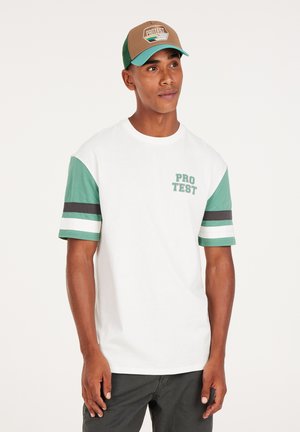 Witte t-shirt met korte mouwen en groene patroonsleeves, voorzien van een 'PRO TEST' grafiek op de borst. Draag het met een bruine en teal honkbalpet.