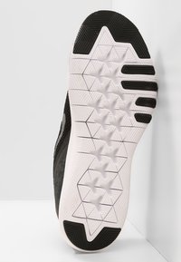 Černá podrážka atletické obuvi s texturovaným bílým povrchem, obsahující šestihranné a trojúhelníkové vzory pro lepší trakci. Čistý design a odolný materiál.