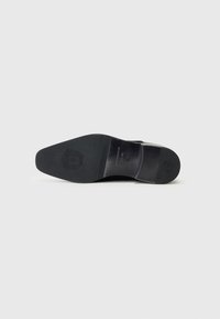 Black leather shoe sole with a sleek, curved shape. Features engraved logo, textured patterns, and a tapered heel for a refined design.