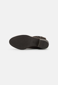 Brauner Lederstiefel mit einer strukturierten Gummisohle im Wabenmuster. Seitliche Akzentdetails umfassen metallische Beschläge.