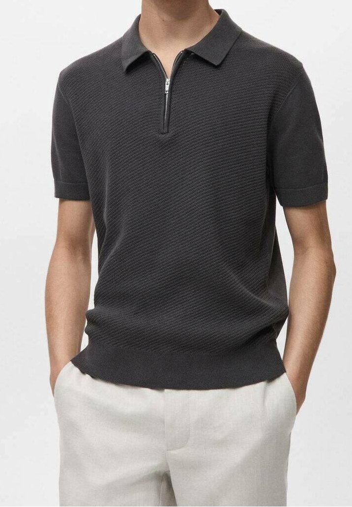 Polo à manches courtes gris foncé en tissu tricoté texturé, avec un col zippé et une coupe cintrée. Porté avec un pantalon de couleur claire.