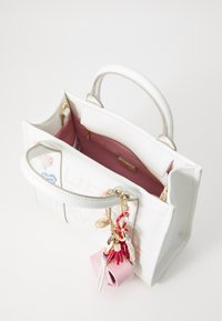 Borsa bianca con un design strutturato, dotata di un interno rosa, hardware dorato e dettagli di charm colorati attaccati al manico.