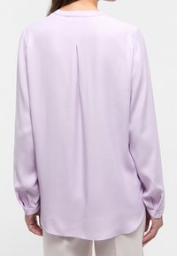 Svetle fialová halenka s dlouhými rukávy, kulatým výstřihem, jemnou texturou a záložkou na zadní straně pro pohodlný pohyb. Manžety na knoflíky dodávají detail.