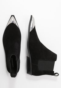 Botines negros de ante con puntera puntiaguda, puntera metálica plateada, paneles laterales elásticos y un pequeño tacón cuadrado.