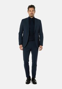 Marineblauw pak met een slim fit, enkelzijdig jasje, notch revers, bijpassende gilet en zwarte dress schoenen. Gladde stof textuur.