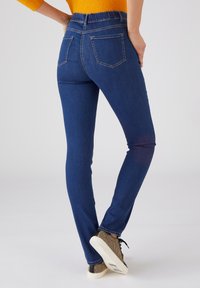 Pantalones vaqueros ajustados en denim azul oscuro con textura suave, que presentan una cinturilla alta elástica, cinco bolsillos y costuras en contraste.