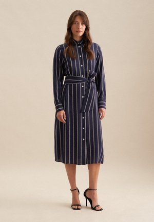Marine gestreepte blousejurk met een ceintuur in de taille, voorzien van lange mouwen en contrasterende lichtgekleurde verticale lijnen. Glad materiaal met een gepolijste afwerking.