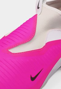 Κοντινό πλάνο ροζ και λευκού παπουτσιού Nike με υφασμάτινη επιφάνεια και μαύρο λογότυπο swoosh στο πλάι.