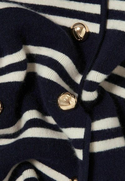 Maglione a righe blu navy e bianche, caratterizzato da grandi bottoni dorati, una consistenza morbida e un aspetto leggermente sgualcito del tessuto.