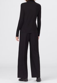 Zwarte langemouwtop gecombineerd met losse zwarte broek. Gladde textuur, minimalistisch ontwerp en geen zichtbare patronen of accenten.