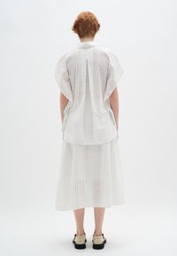 Completo in cotone bianco composto da una maglietta ampia con un motivo a intaglio e una gonna lunga coordinata, entrambi con una finitura testurizzata e una vestibilità comoda.