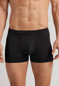 Černé boxerky vyrobené z hladkého, elastického materiálu. Mají přiléhavý střih s podpůrným předním vakem a elastickým pasem.