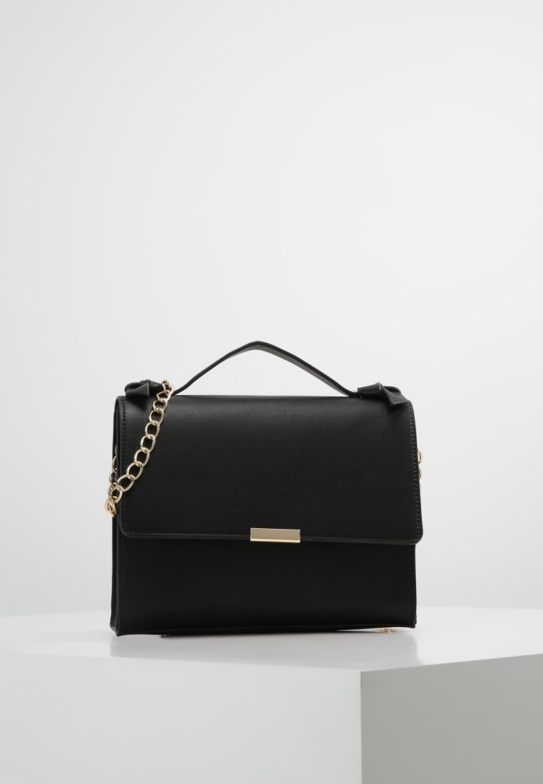 Černá kožená kabelka s pevným tvarem, zlatým řetízkovým popruhem a přední klopou s kovovým akcentem. Hladká textura, elegantní provedení.