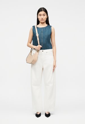 Naine kannab varrukateta teksatoppi, valgeid laiade jalgadega pükse, musti teravnurkseid kingi ning kannab beežikat õlakotti, millel on ketiga detail.