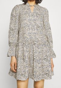 Klänning med mönstrad tyg i krämfärgad, marinblå och beige, med lång ärm, nyckelhålsringning och rynkad midja.