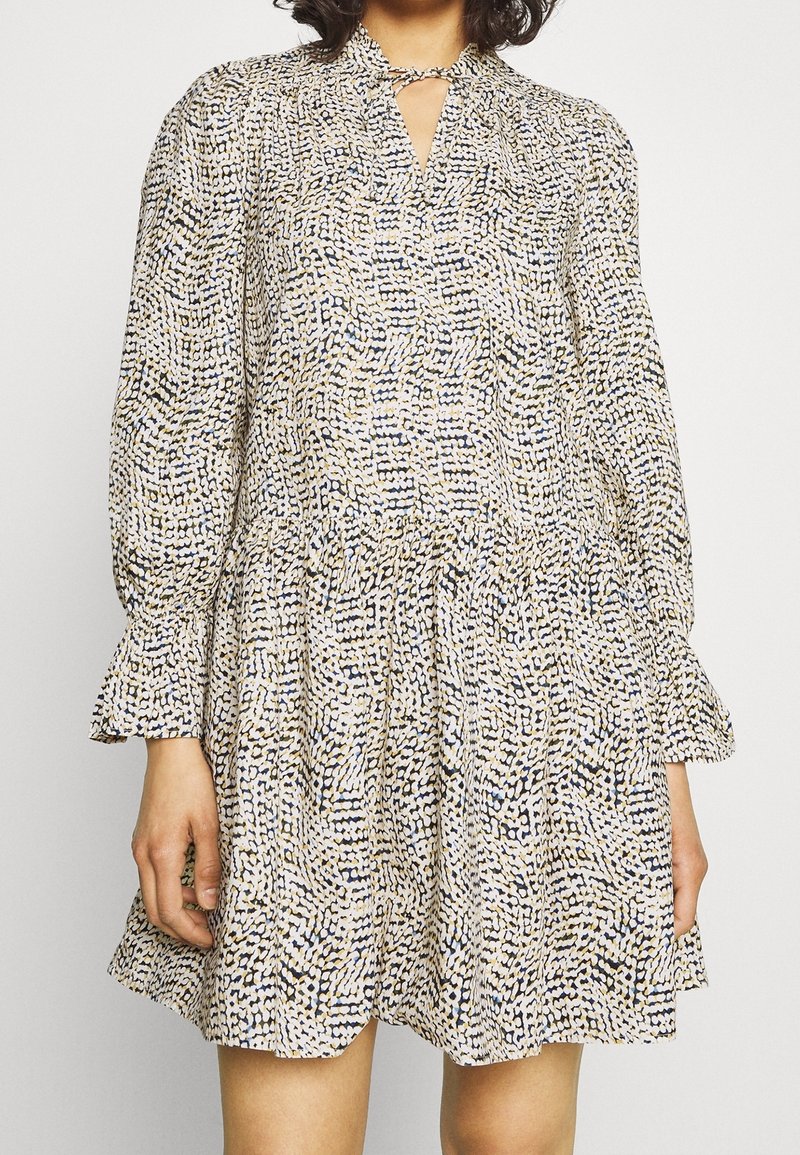 Klänning med mönstrad tyg i krämfärgad, marinblå och beige, med lång ärm, nyckelhålsringning och rynkad midja.