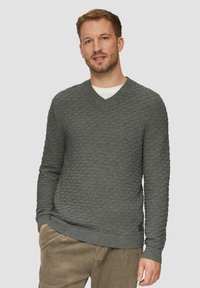 Grauer gestrickter Pullover mit Rautenmuster, V-Ausschnitt, gerippten Manschetten und Saum, kombiniert mit hellbraunen Cordhosen.