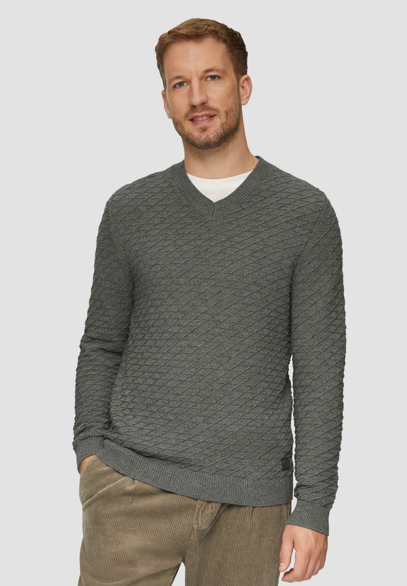 Grauer gestrickter Pullover mit Rautenmuster, V-Ausschnitt, gerippten Manschetten und Saum, kombiniert mit hellbraunen Cordhosen.