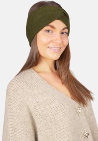 Bandeau tricoté vert olive avec un design torsadé. La texture est douce et solide, assortie à un cardigan tricoté beige clair avec des boutons dorés.