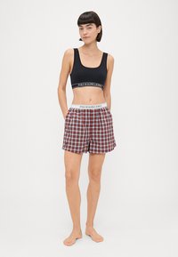 Μαύρο αθλητικό σουτιέν με λογότυπο στη ζώνη και κόκκινες καρό βερμούδες με ελαστική μέση, κουμπί και χαλαρή εφαρμογή.