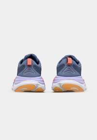 Blaue Sportschuhe mit einem strukturierten Mesh-Obermaterial, ausgestattet mit einem rosa Fersensporn und einer wellenförmigen lavendel-farbenen Zwischensohle. Orangefarbige Gummisohle mit Traktionsmustern.