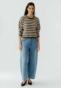 Gestreifter Pullover in Grün und Pink, kombiniert mit weit geschnittenen blauen Jeans. Das Outfit zeichnet sich durch eine lockere Passform und einen runden Halsausschnitt aus.