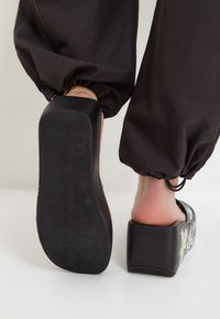 Pantofi platformă negri cu un brant texturat și un design grafic colorat. Prezintă un spate deschis și un toc gros pentru un plus de înălțime.