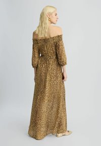 Schoudervrije lange jurk van bruine stof met een luipaardprint, met losse mouwen en een verstelbare taille. Transparante textuur.