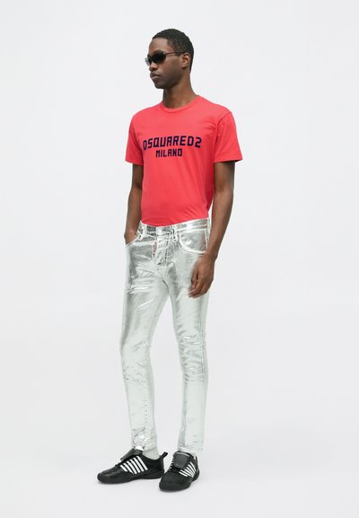 Punane lühikeste varrukatega T-särk musta "DSquared2 MILANO" logoga, kombineeritud metallik hõbedaste teksade ja mustade tossudega, millel on valged triibud.
