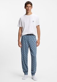 Witte katoenen T-shirt met een borstzak, gecombineerd met blauwe pyjamabroek met patroon, voorzien van een elastische tailleband en omgeslagen pijpen.