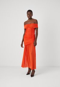 Κούκλα πορτοκαλί φόρεμα off-the-shoulder με ruched ύφασμα, μάκρος έως το πάτωμα, διάφανη φούστα και εφαρμοστό μπούστο. Συνδυασμένο με μαύρες ψηλές γόβες.