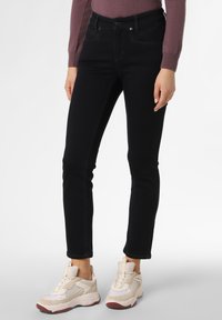 Osoba v černých slim-fit džínech, mauve dlouhém rukávu a béžových chunky teniskách stojící na bílém pozadí.