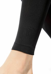 Sorte leggings i stretchstof med en glat tekstur, der har en diskret logo trykt nær anklen og et tætsiddende design.