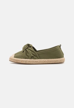 Olijfgroene instap-espadrille met jutes zool en een geknoopt stoffen detail aan de voorkant, geplaatst tegen een effen lichte achtergrond.
