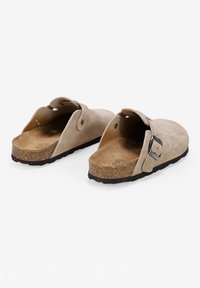 Mules de ante en beige claro con espalda abierta, correa ajustable, suela de corcho y plantilla texturada para mayor comodidad.